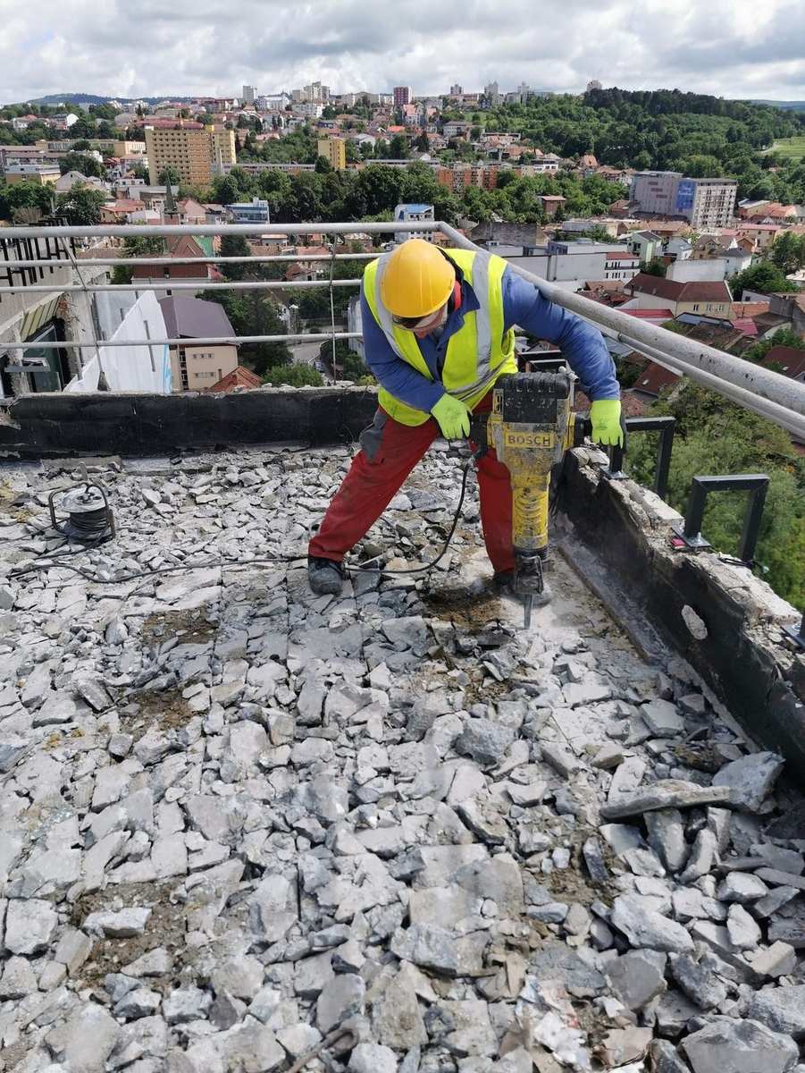 Worker using a Bosch demolition hammer to remove a flat-roof surface on a tall building